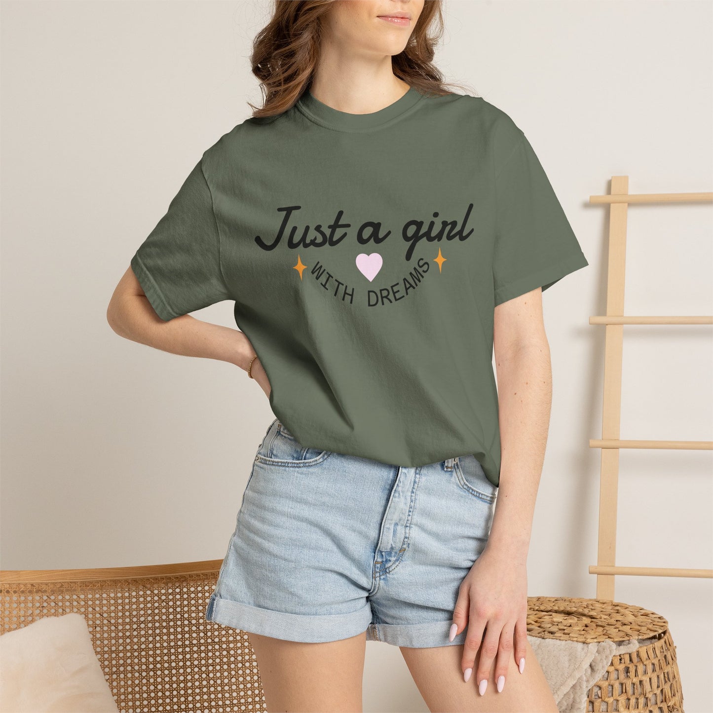 Woman wearing an olive green t-shirt with 'Just a girl WITH DREAMS' illustration and denim shorts.