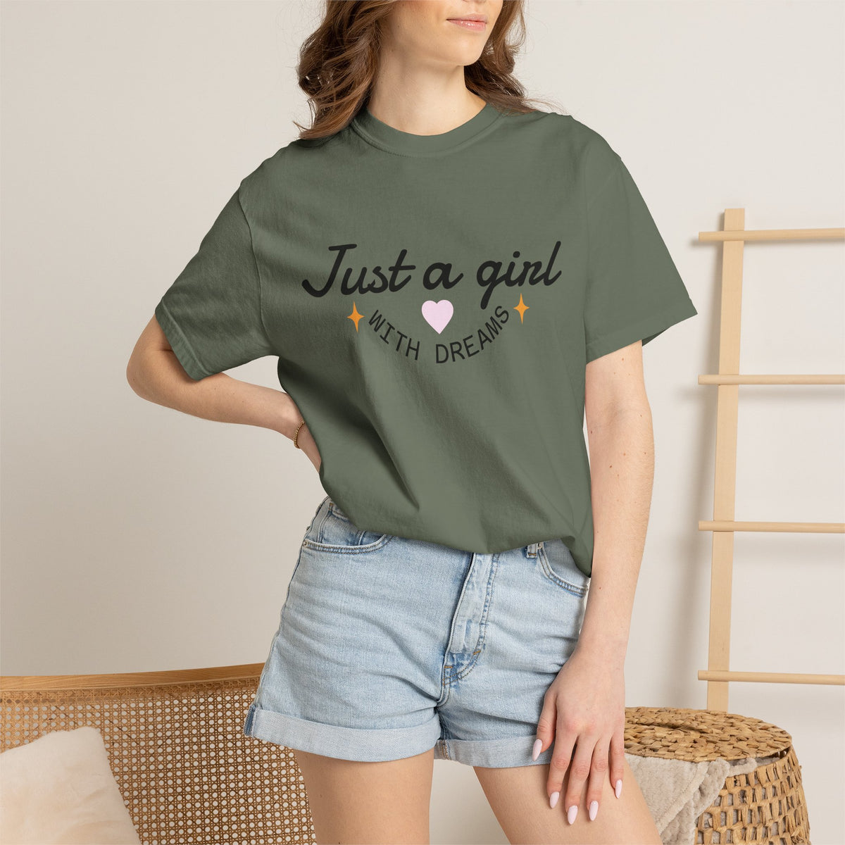 Woman wearing an olive green t-shirt with 'Just a girl WITH DREAMS' illustration and denim shorts.