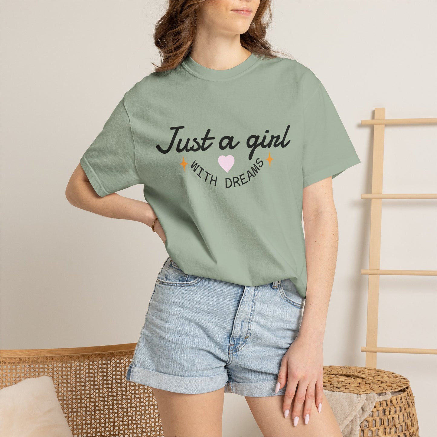Woman wearing a sage green t-shirt with 'Just a girl with dreams' illustration and denim shorts.
